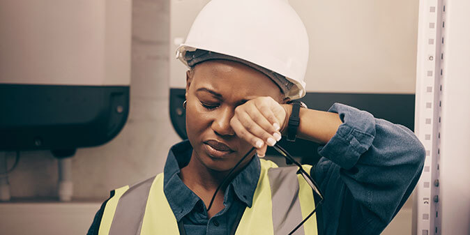 Burntout worker in hardhat, wiping her brow
